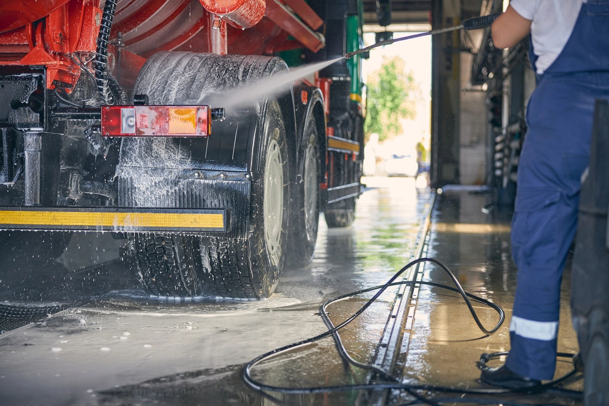 Worker washing red truck with hose
