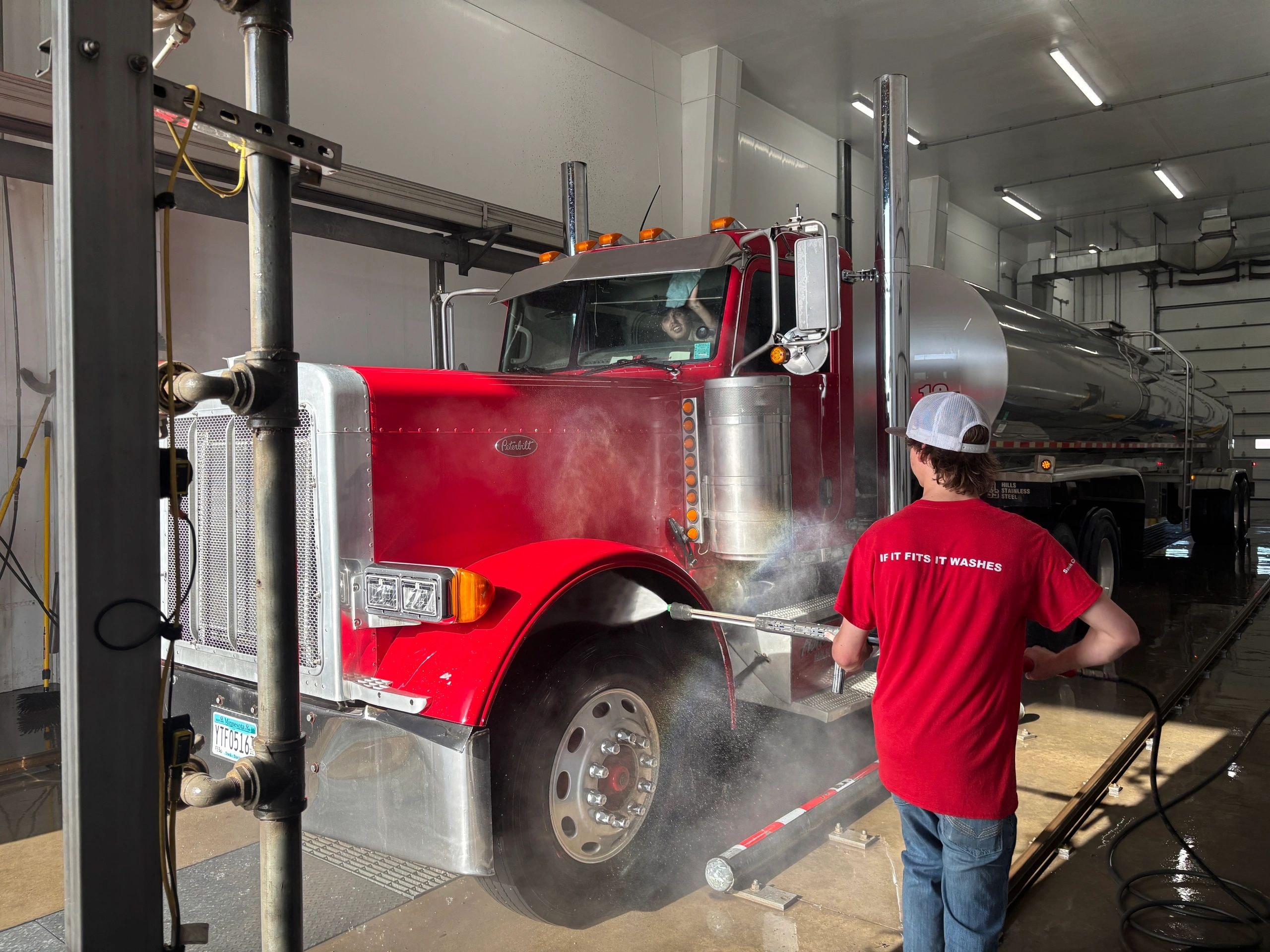 Worker washing red semi truck in wash bay